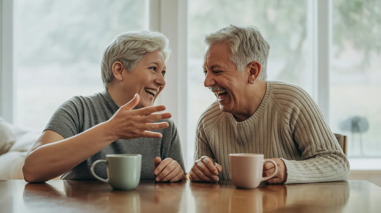 An older man and woman are seated at a kitchen table, laughing together warmly in bright, soft daylight from a window.