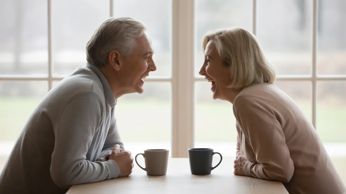 An elderly man and woman share a laugh over coffee at their sunlit kitchen table, enjoying a moment of connection.