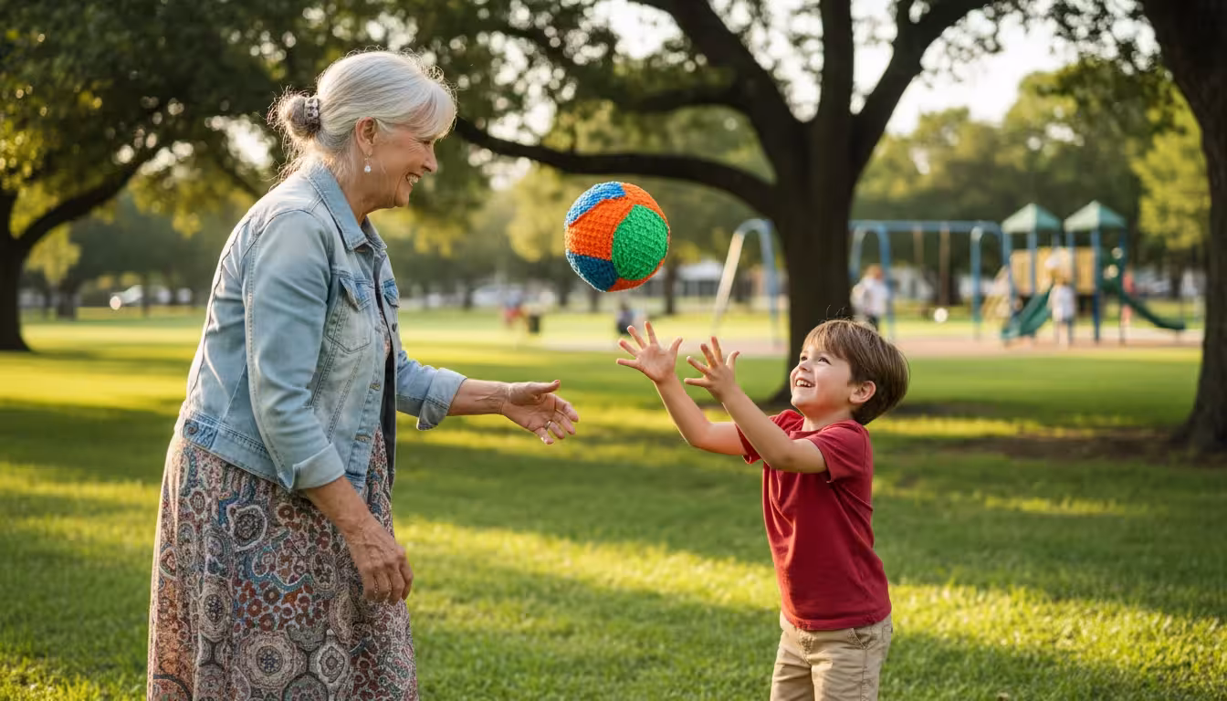A senior woman with a warm smile tosses a colorful ball to her grandchild in a sunny park, both laughing.