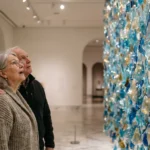 An older couple looking at a large blue and gold glass art installation in a bright, modern museum gallery.