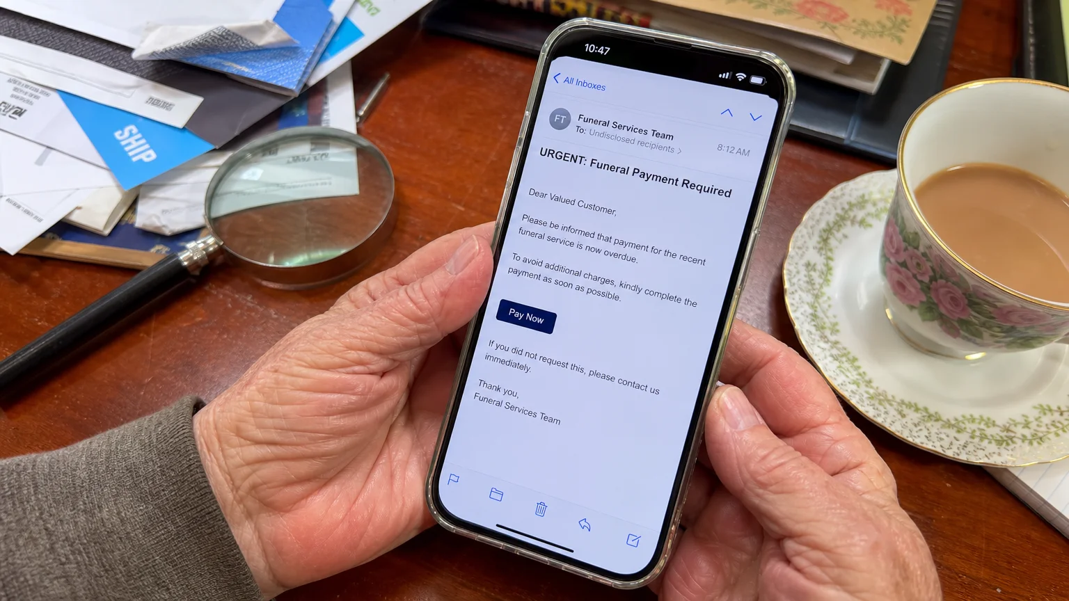 A close-up snapshot of a senior's hands holding a smartphone showing a suspicious funeral-related email.